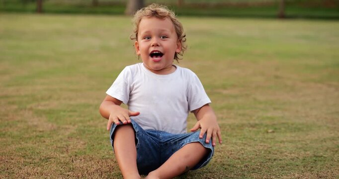 Little boy sits and sings loudly, slapping his hands in rhythm on his knees. He shouts and screeches with excitement, fully immersed in his playful performance.