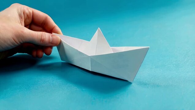 Charming and pristine 4K video showing a clean white origami paper vessel gliding smoothly across a calm blue background offering generous copy space for conceptual themes of childhood education and