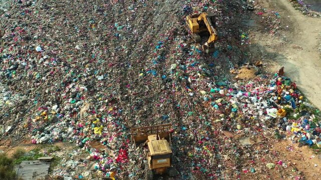 Aerial view of bulldozers managing large plastic waste landfill and pollution site.