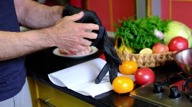 A chef puts on black disposable gloves before handling fresh ingredients and cooking. Professional kitchen preparation begins with clean hands and proper food hygiene.