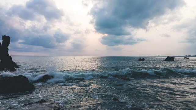 Scenic rocky beach landscape with a unique rock formation pillar and sea waves at sunset
