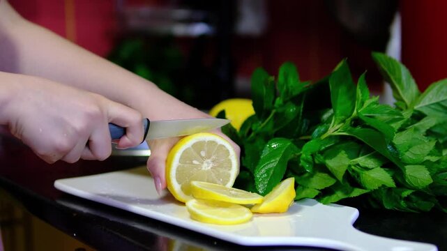 Fresh citrus is carefully cut into thin slices while aromatic mint waits nearby for refreshing recipes. Bright ingredients are prepared for homemade drinks and desserts.
