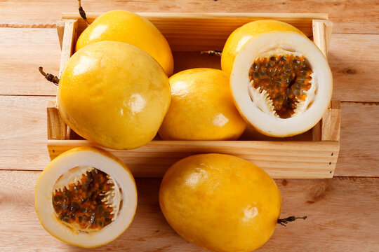 Whole and cut yellow passion fruit displaying fresh pulp and seeds in a rustic wooden crate on a wooden table