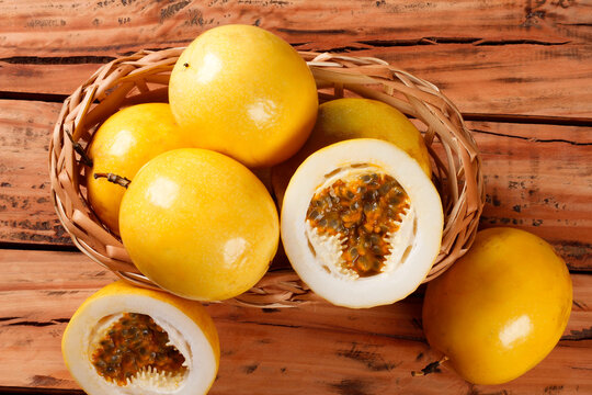 Whole and cut yellow passion fruits revealing fresh pulp and seeds on a wicker basket on a rustic wooden table
