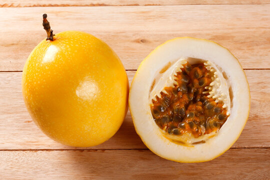 Whole yellow passion fruit next to a cut half revealing fresh pulp and seeds on a light wood surface