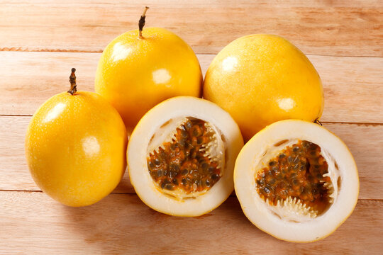 Group of whole and cut yellow passion fruits highlighting fresh pulp and seeds on a light wood table.