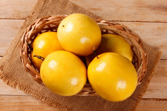 Wicker basket with fresh yellow passion fruit on jute fabric and a light wood surface.