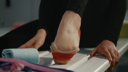Close Up of Rhythmic Gymnast Foot in Specialized Half Socks Inside Changing Room. Athlete Meticulously Ties Red Elastic Resistance Band Around Arch and Ankle, Likely For Injury Prevention, Support. © Framestock