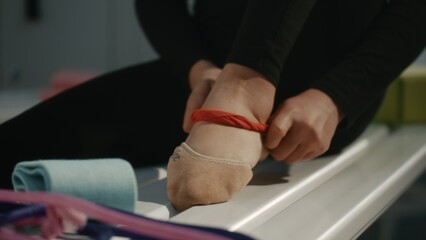 Close Up of Rhythmic Gymnast Foot in Specialized Half Socks Inside Changing Room. Athlete Meticulously Ties Red Elastic Resistance Band Around Arch and Ankle, Likely For Injury Prevention, Support. © Framestock