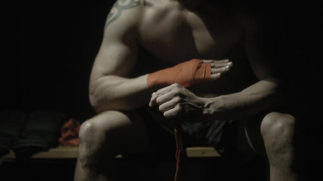 Shirtless boxer wrapping hands in dramatic low key light