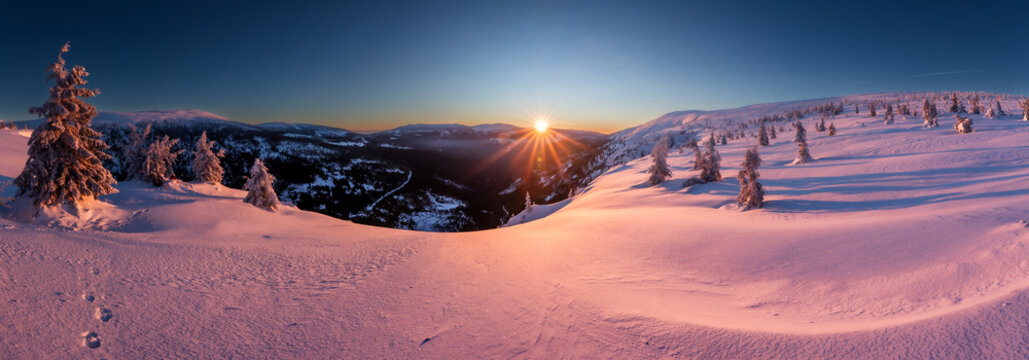 Vibrant pink and orange alpenglow sky over snow-covered winter mountain ridges, Krkonose.