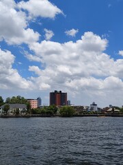 Fototapeta premium Scenic view of the Chao Phraya River with the Bangkok city skyline and a bright blue sky filled with white clouds.
