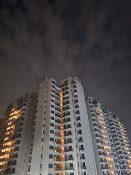 A modern residential building illuminated at night under a cloudy sky, showcasing a blend of urban architecture and atmospheric lighting that evokes a calm yet lively mood.