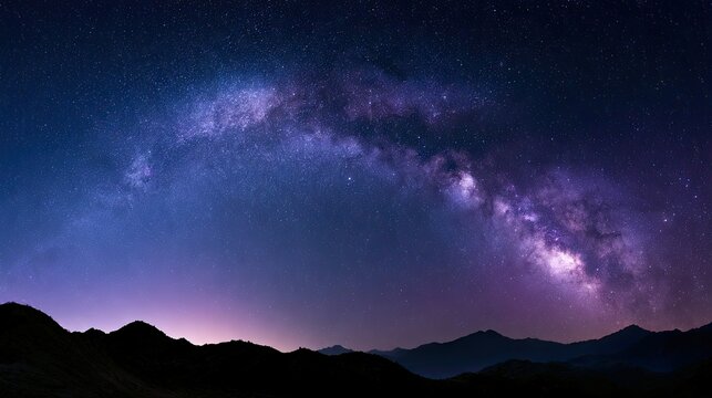 Vast starry night sky with luminous galaxy arching over dark, silhouetted mountains