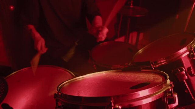 Tilt up shot of Caucasian man playing drums in recording studio under red light. Clip for music school commercials, band promotions, or entertainment industry marketing videos