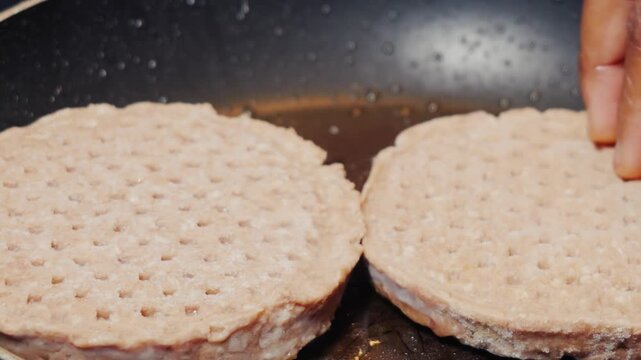 Close up action shot of burger meat rounds being tossed by shaking a nonstick pan