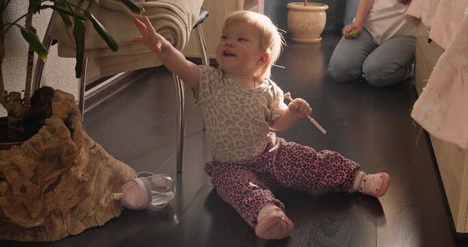 Toddler sitting on the floor and reaching toward a houseplant during everyday play at home. Early curiosity and exploration in a domestic environment