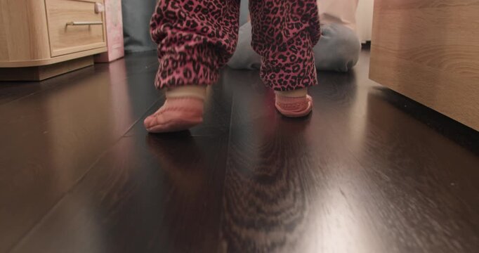 Toddler girl taking first unsteady steps at home. Early childhood milestone and motor skill development