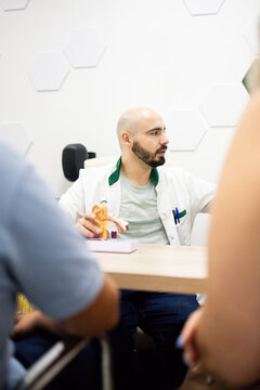 Vertical photo of ENT doctor explaining ear anatomy model to couple during medical consultation in clinic.Concept of otolaryngologist.