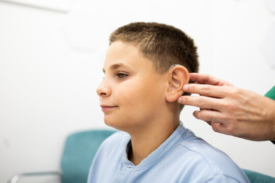 Child wearing a behind-the-ear hearing aid while a professional adjusts the device in a clinical setting. Concept of hearing health, medical technology, hearing loss, rehabilitation, and healthcare.