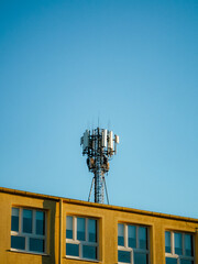 Anteny telefonii komórkowej na maszcie nad dachem żółtego budynku © Szymon