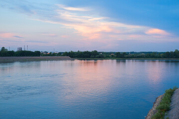 Fototapeta premium River landscape at dusk with calm water, pastel sky, and gentle reflections across the wide river, trees along the bank.