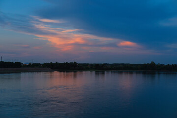 Fototapeta premium Sunset over a calm river with reflective water, clouds across the sky, creating a peaceful horizon and tranquil evening landscape scene