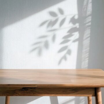 Empty wooden table top close up view with soft tropical leaf shadow on white wall background representing minimalist copy space