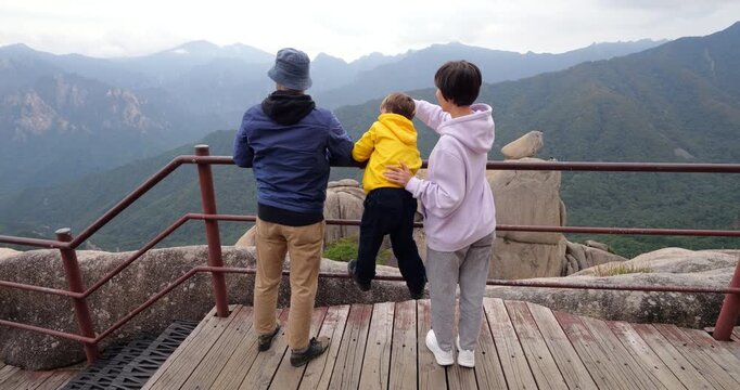 Family tourists admiring breathtaking landscape from Ulsanbawi summit viewpoint, back view. Woman and boy pointing at distant peaks in awe of the scenic mountain panorama of Seoraksan National Park.