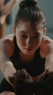 Girl in Athletic Outfit Performs Deep Forward Bend Stretch in Warm Up, Improving Hamstring Flexibility, Spinal Mobility. Training Routine, Required in Competitive Youth Gymnastics. Vertical Shot.