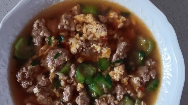 A video close up of Luffa or Sponge Gourd and Egg Soup with Minced Chicken on a white bowl.