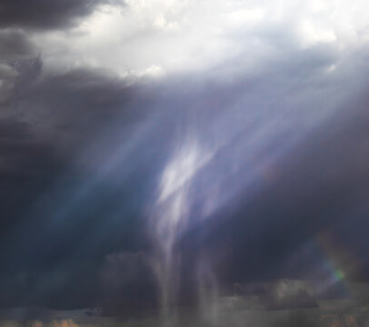 Rain shafts illuminated by sunbeams with a small rainbow