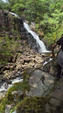 Male tourist exploring Pistyll Cain waterfall in Coed y Brenin Forest, Snowdonia National Park, North Wales, United Kingdom