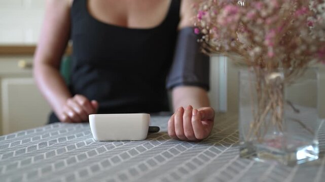 Woman measuring blood pressure with digital monitor at home.