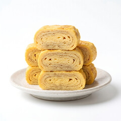 Fototapeta premium Stacked slices of Japanese tamagoyaki, a savory rolled omelet, on a white plate against a clean white background, showcasing layers of cooked egg