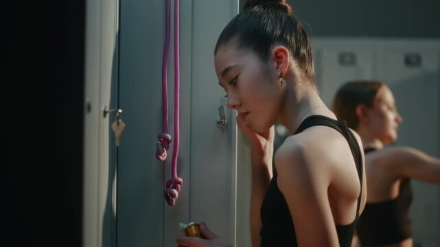 Young Female Athlete in Locker Room Inserts Wireless Earbud to Ear and Looks Smartphone, Eagerly Preparing to Play Audio Voice Message From Friend. Modern Teen Communication Everyday Sports Lifestyle.