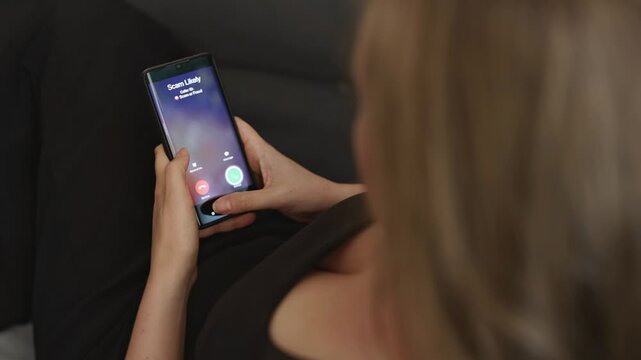 Woman holding smartphone with incoming scam call on screen.
