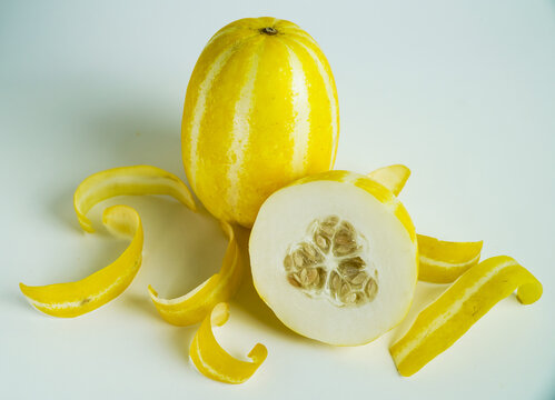 Yellow Striped Melon Cut in Half with Seeds and Peels on White Background