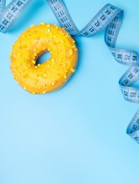 Measuring tape surrounding colorful donut highlights body measurement and calorie awareness in clean composition. Measuring progress fits fitness campaigns, nutrition education, wellness branding 