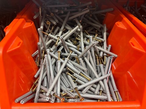 Orange bin filled with grey plastic wall plugs and metal screws in a hardware store. DIY projects, home improvement, construction, and hardware store supplies.
