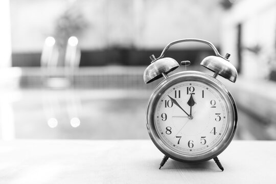Old vintage alarm clock on swimming pool edge with space on blurred background, timeline and deadline background idea, black and white filter effect