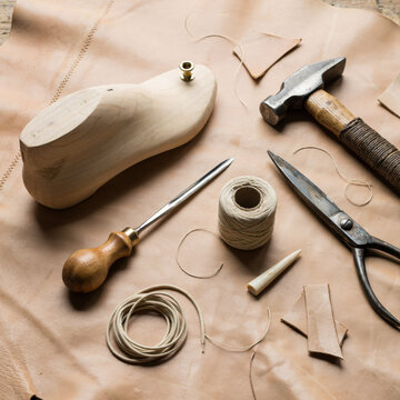 Cobbler's tools and wooden last arranged on tanned leather during a craft process for shoe repair