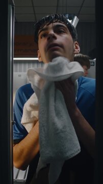 Sweaty Teenage Soccer Player Opening Door After Workout. Young Man Wipes Face With Towel, Takes Refreshing Drink of Water From Sports Bottle, Closes Locker Door. Post Game Exhaustion. Vertical Shot.