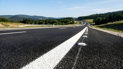 Obraz premium Asphalt Road with White Lane Markings Extending into Scenic Countryside under Clear Sky