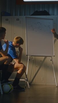 Football Mentor Points Tactical Board While Lecturing Youth Team at Half Time or Before Training. Teenage Student Athletes Listen Carefully. Leadership, Team Discipline, Sportsmanship. Vertical Shot.