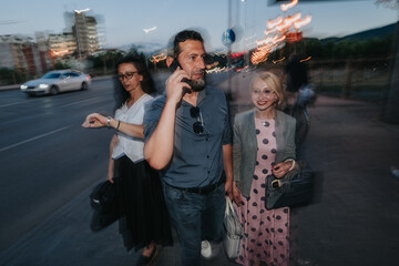 A senior business trio walks along an urban street as a man talks on his phone. Candid evening shot...