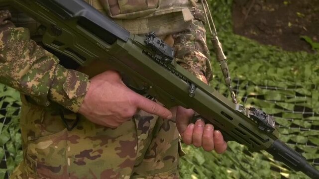 Soldier in camouflage standing guard at a concealed field position under camouflage netting. Military surveillance, security, and defensive operations in a field environment during armed conflict.