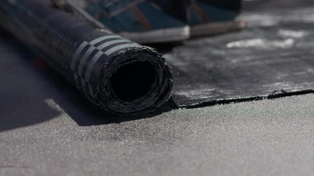 Bitumen roofing membrane unrolled across flat roof before torch welding