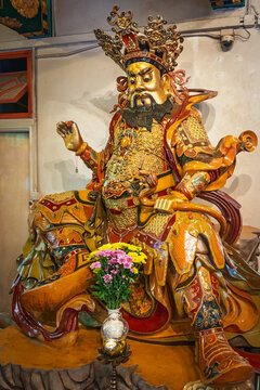 Hong Kong, China. December 10, 2013, Man Mo Temple worshiping a colorful traditional chinese deity statue adorned with intricate detail and gold, with flowers and candle