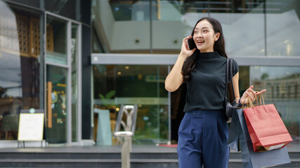 Fototapeta premium Asian woman talking on phone with shopping bags at modern mall, Black Friday, shopping
